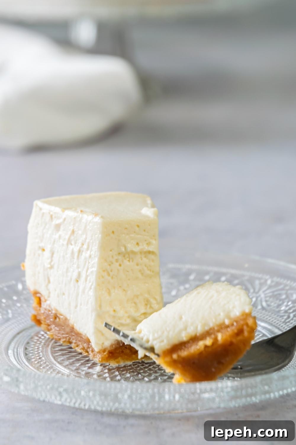 A slice of Philadelphia No Bake Cheesecake on a serving plate. A fork has taken out a bite size of it and is laying next to the slice on the plate.