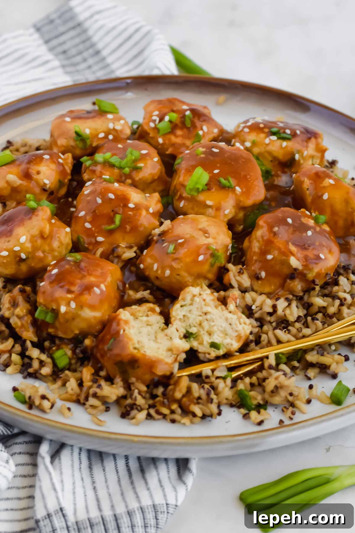 Asian chicken meatballs over bed of rice on white plate with chopsticks.