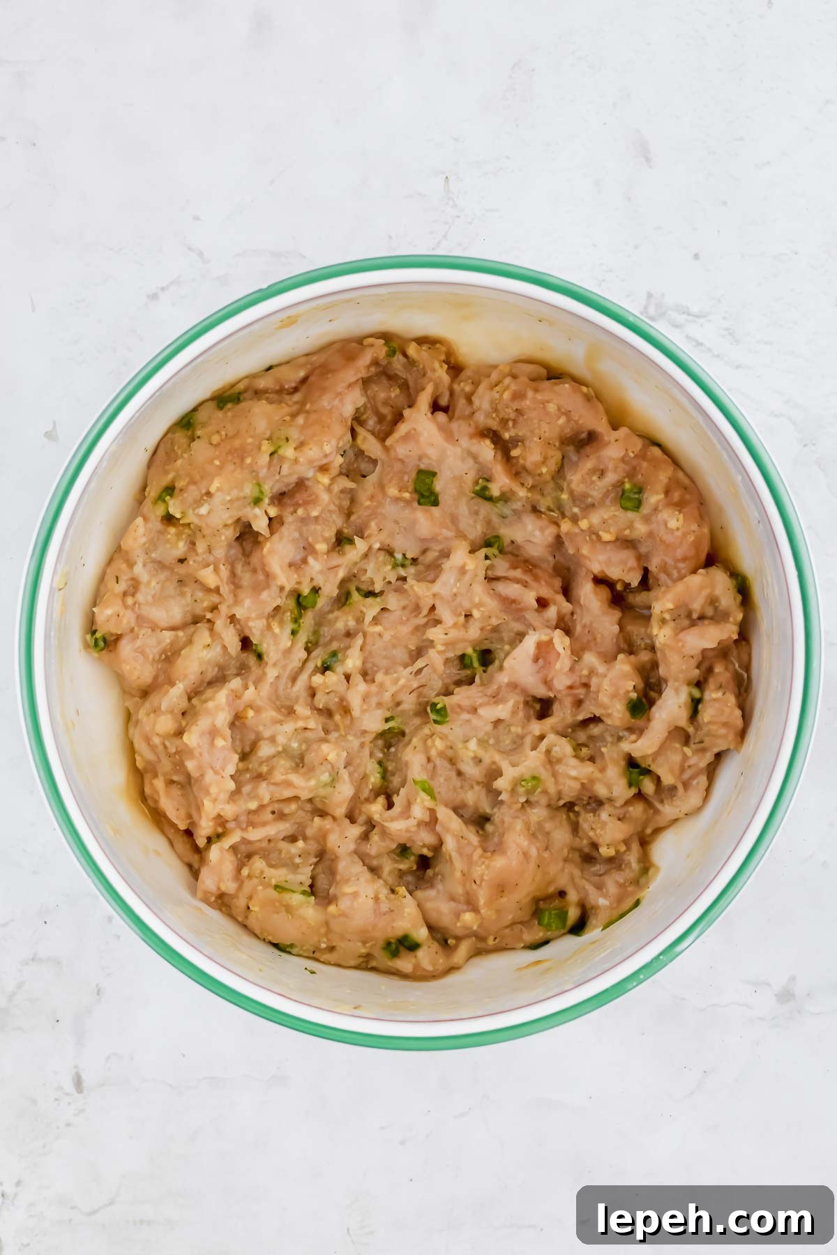 asian chicken meatball ingredients mixed in white bowl on white background.