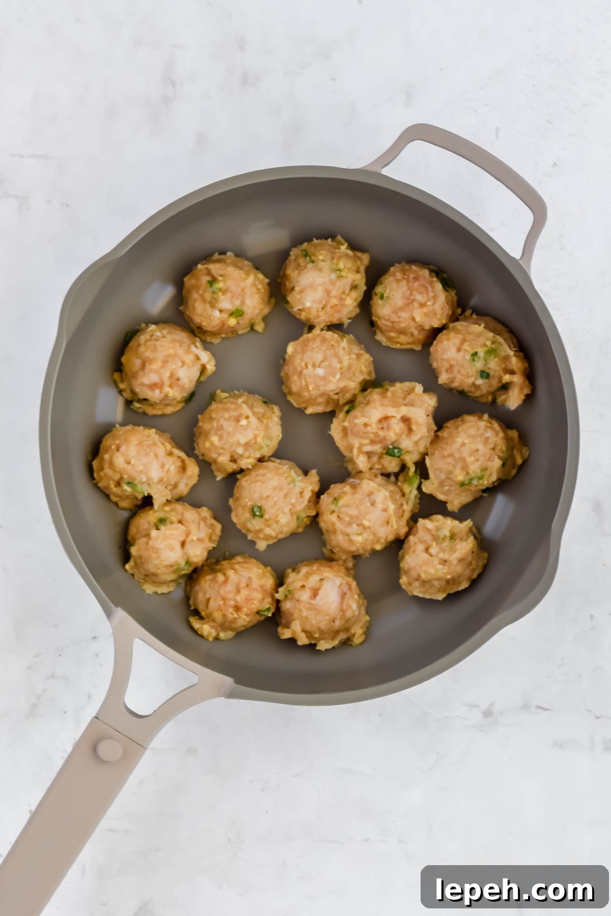 formed raw Asian chicken meatballs in pan on white background.