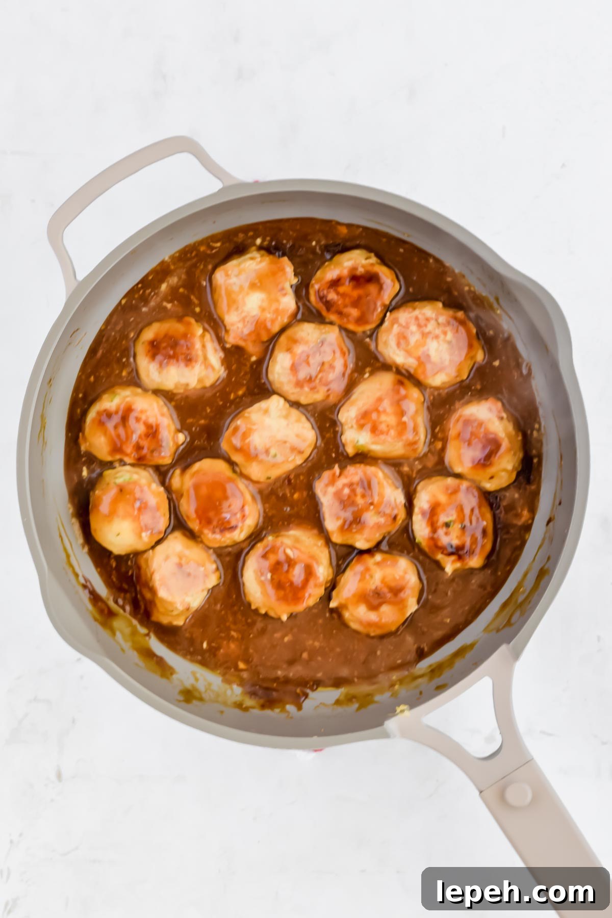 formed raw Asian chicken meatballs with teriyaki sauce in pan on white background.