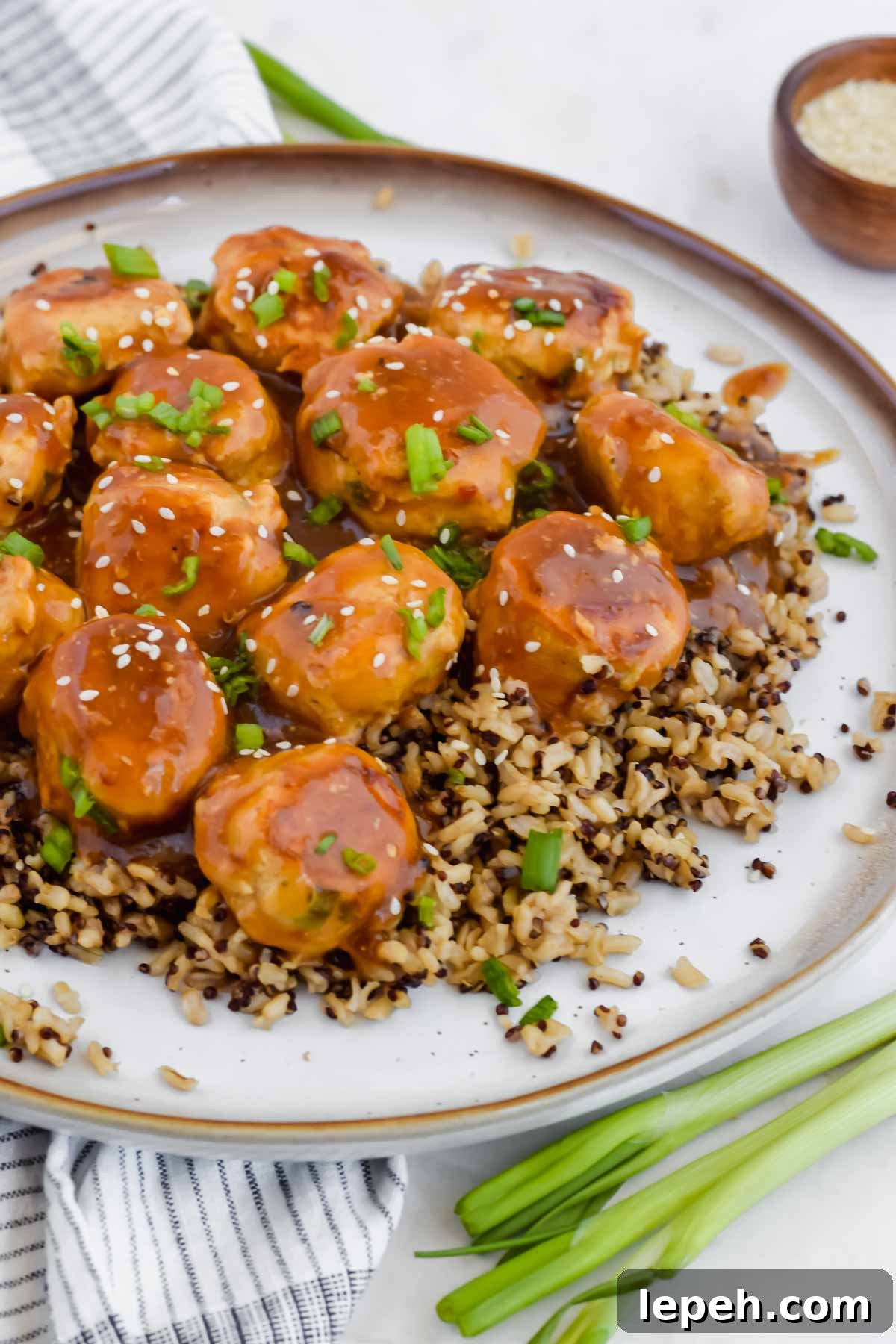 Asian chicken meatballs over bed of rice on white plate and garnished with green onion.