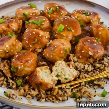 Asian chicken meatballs over bed of rice on white plate with chopsticks.