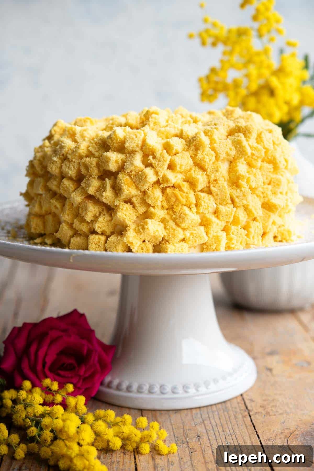 A mimosa cake on a cake stand with mimosa flowers in the background.
