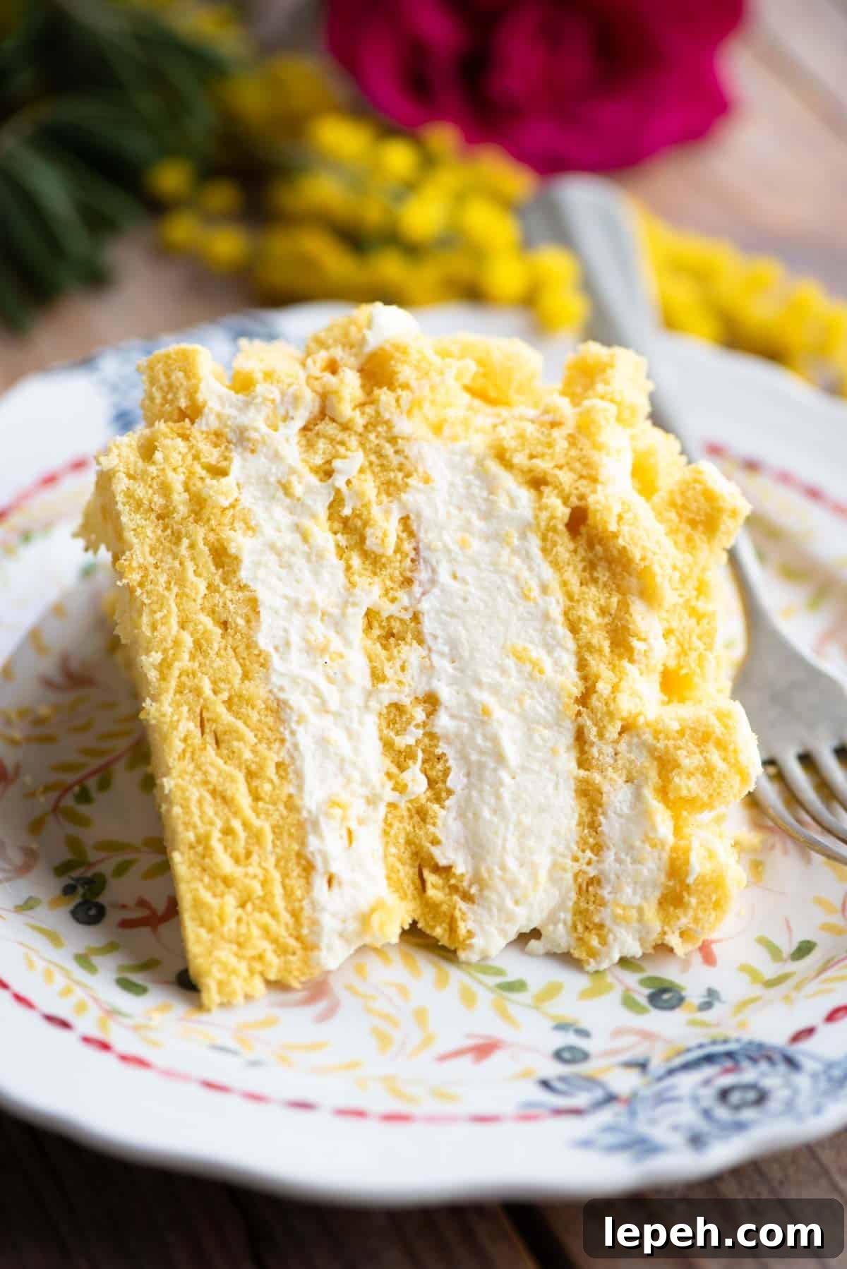 A slice of mimosa cake with three layers and filled with cream on a small plate.