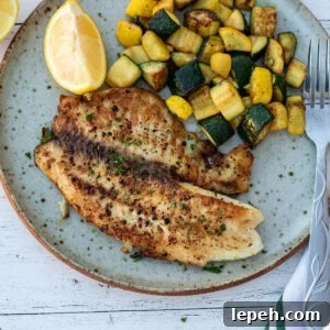 Lemon pepper tilapia on a plate with sautéed zucchini.