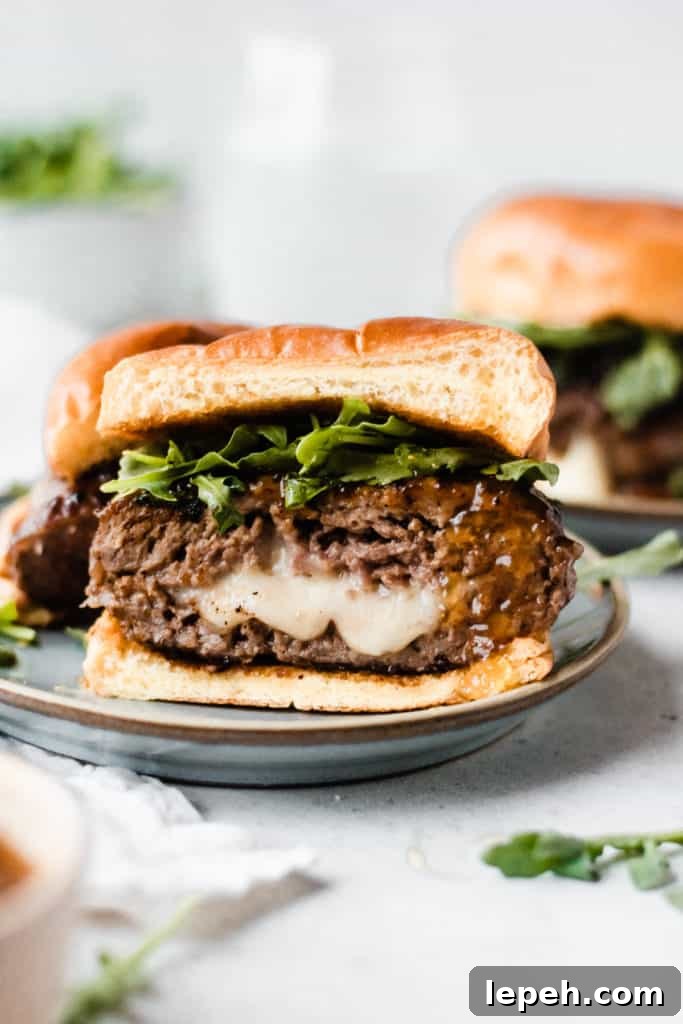 A burger cut on half sitting on a plate, with cheese oozing out, and arugula and fig preserves on the burger