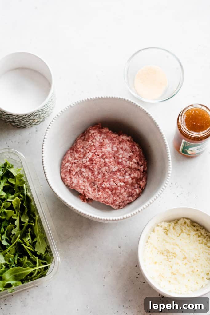 Ingredients for the burgers set out on a surface - salt, garlic powder, a jar of fig preserves, arugula, lamb meat, and mozzarella