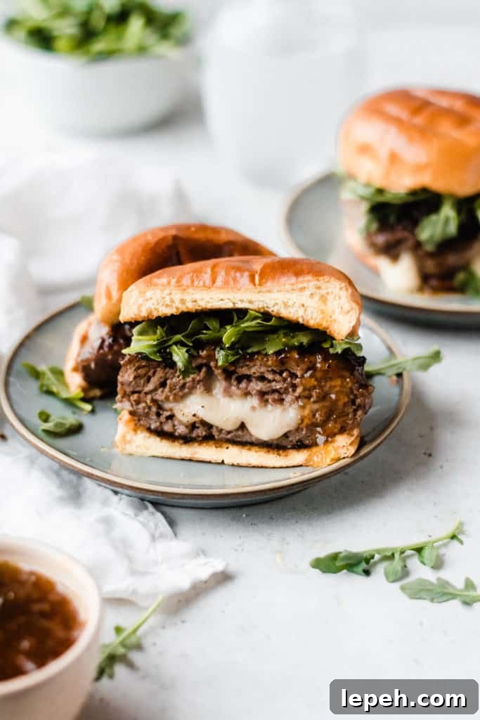 A lamb burger cut in half, with cheese oozing out, topped with fig preserves and arugula, with a brioche bun, on a blue plate