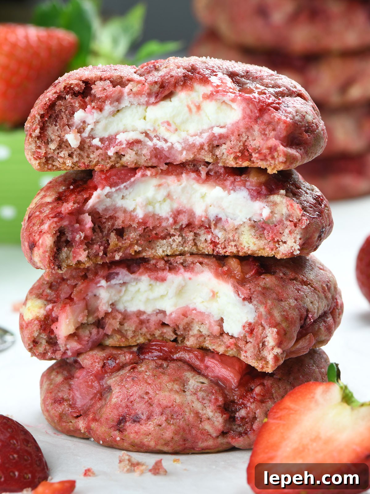 Close-up of strawberry cheesecake cookies stacked on top of each other, revealing a creamy cheesecake filling inside a soft, strawberry-infused cookie. Fresh strawberries are scattered around.