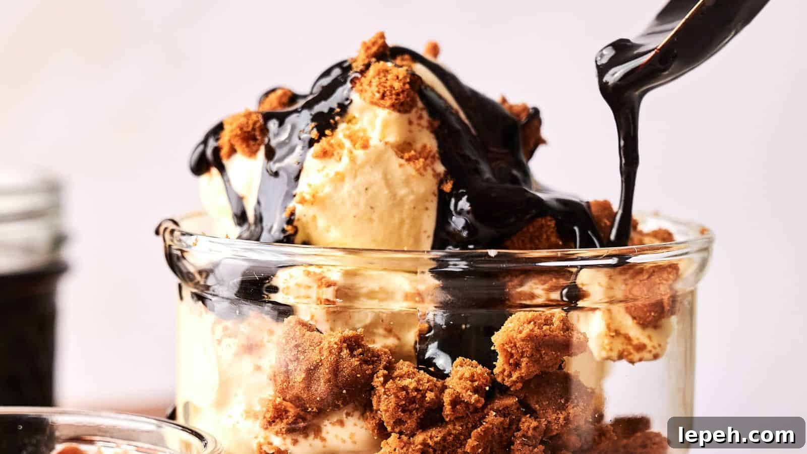 A glass filled with vanilla ice cream, crumbled cookies, and chocolate sauce being poured on top.