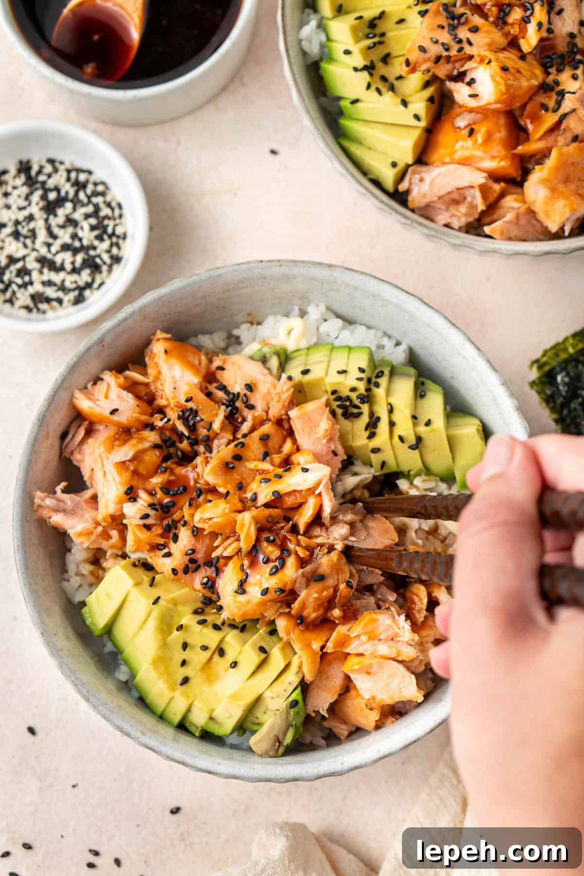 A hand using chopsticks to get a bite of teriyaki salmon and avocado.