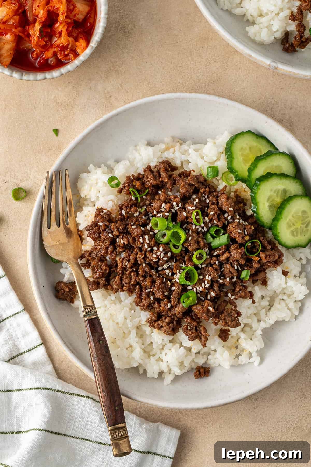 Korean beef bowl with a fork and a side of cucumber.