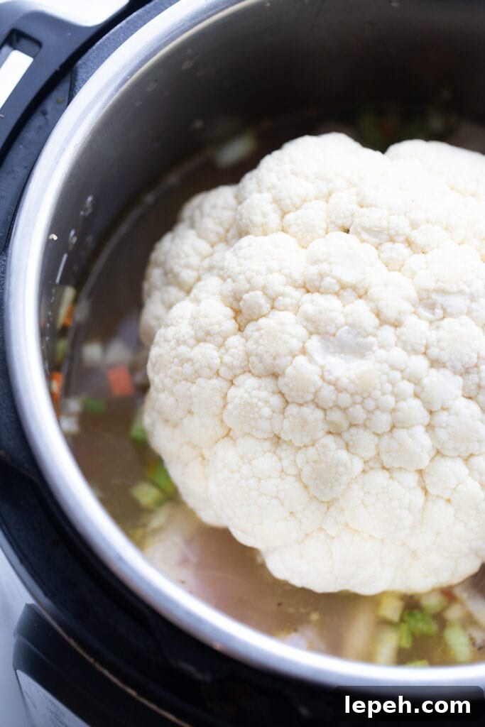 Overhead image: Head of cauliflower on top of chicken and dumplings ingredients, in the Instant Pot.