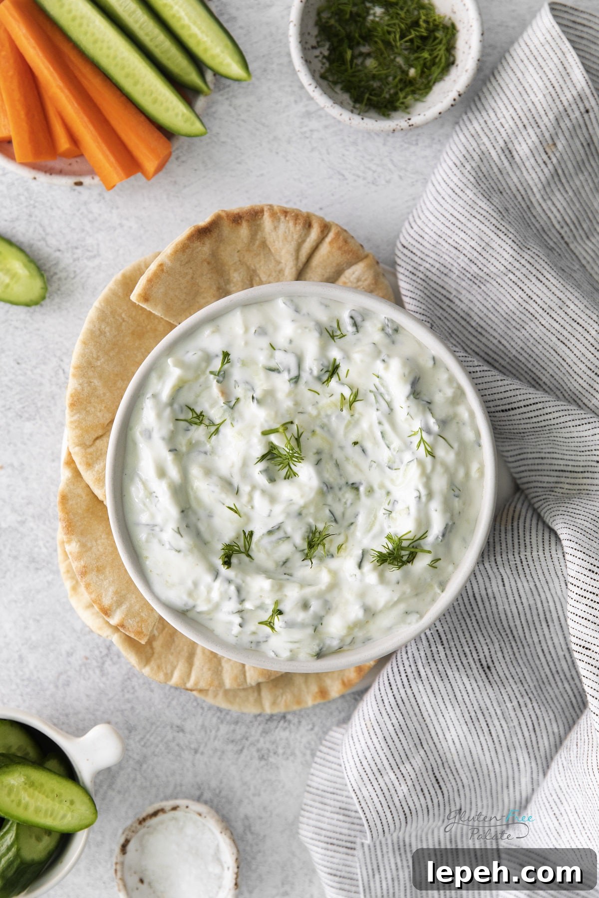 A white bowl of tzatziki dip, viewed from above, served with toasted pita and crudite
