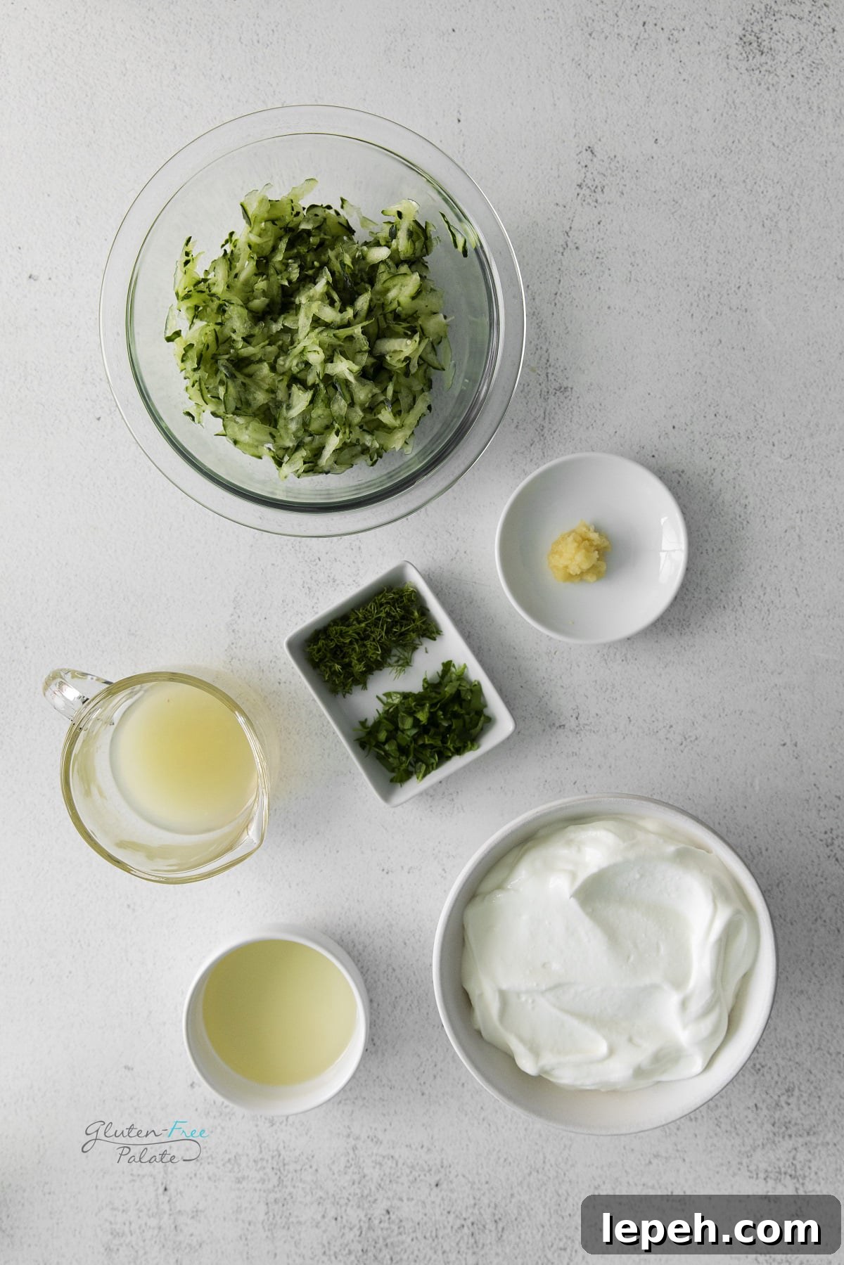 The ingredients for homemade Tzatziki dip, measured into separate small bowls on a concrete counter, viewed from above