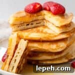 gluten free pancakes in a stack with a piece cut out and strawberries on top with maple syrup being poured on