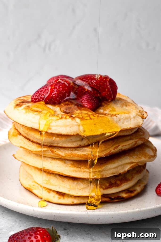 Gluten free pancakes in a stack with syrup being poured over it and strawberries