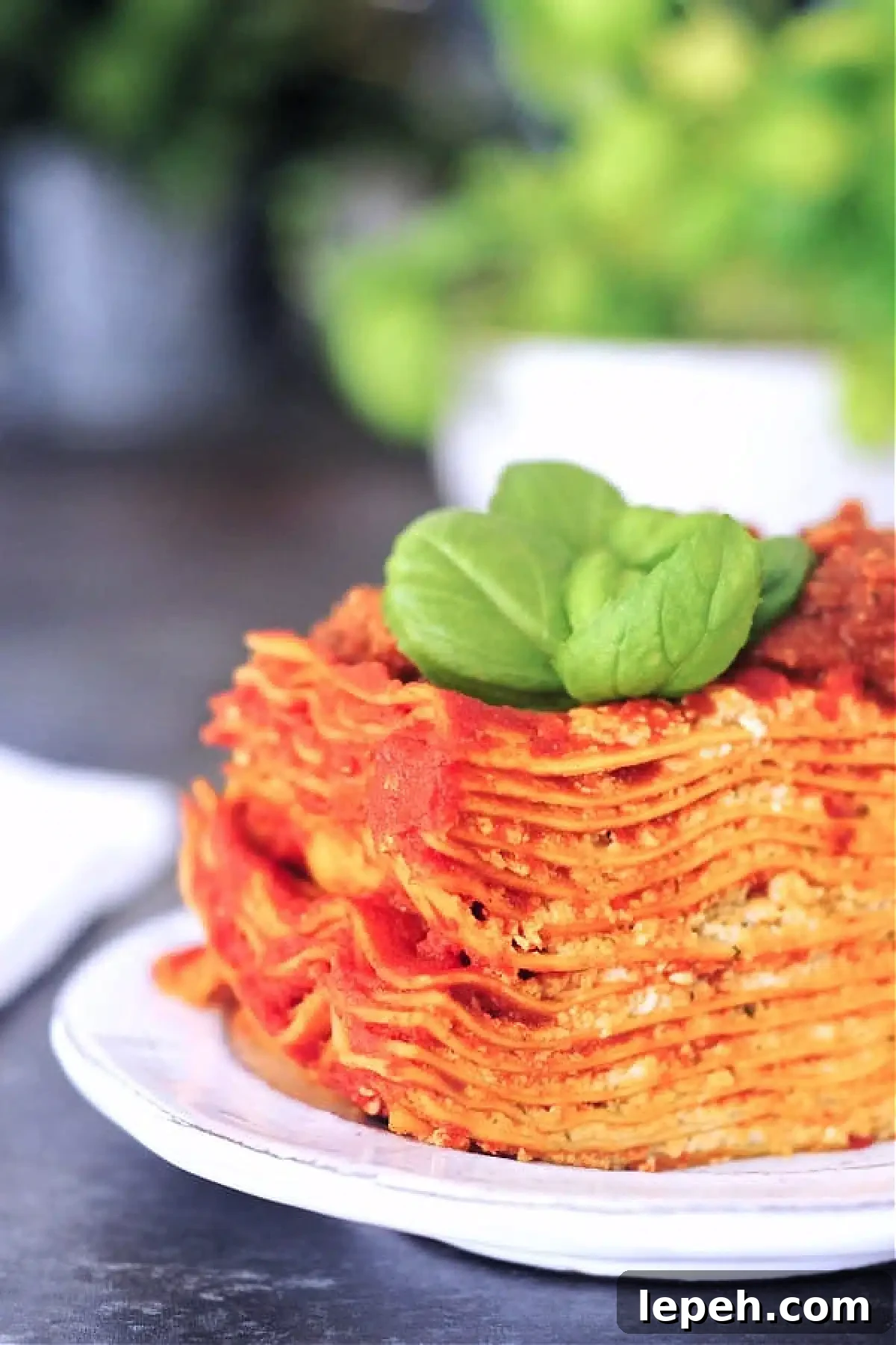 Twelve layer slice of gluten free Vegan Lasagna on a rustic plate, garnished with fresh basil.