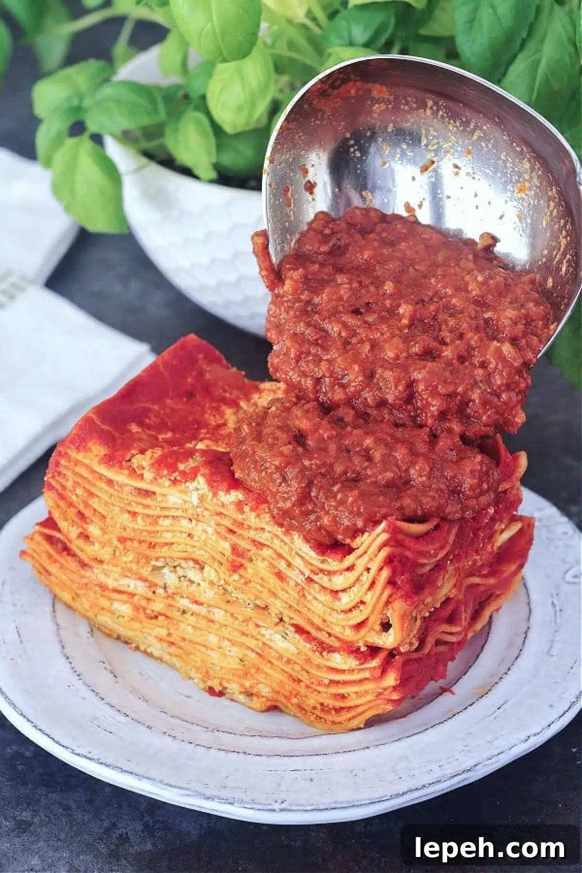 Square of lasagna with meat sauce being poured over top.