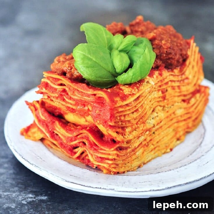 Twelve layer slice of gluten free Vegan Lasagna on a rustic plate, garnished with fresh basil.