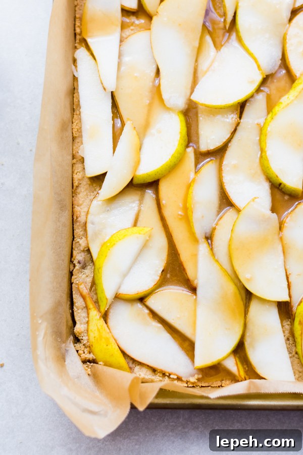 Sliced pears on dough with caramel sauce on a tray.