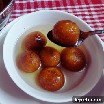 suji ke gulab jamun in a bowl, there are 5 gulab jamun, while another is being held on a spoon above the bowl.