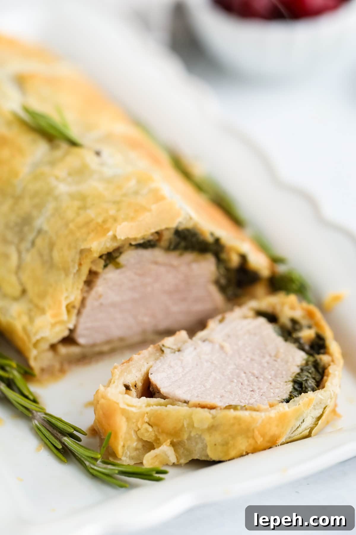 Pork wellington on a plate with slice cut so you can see the inside.