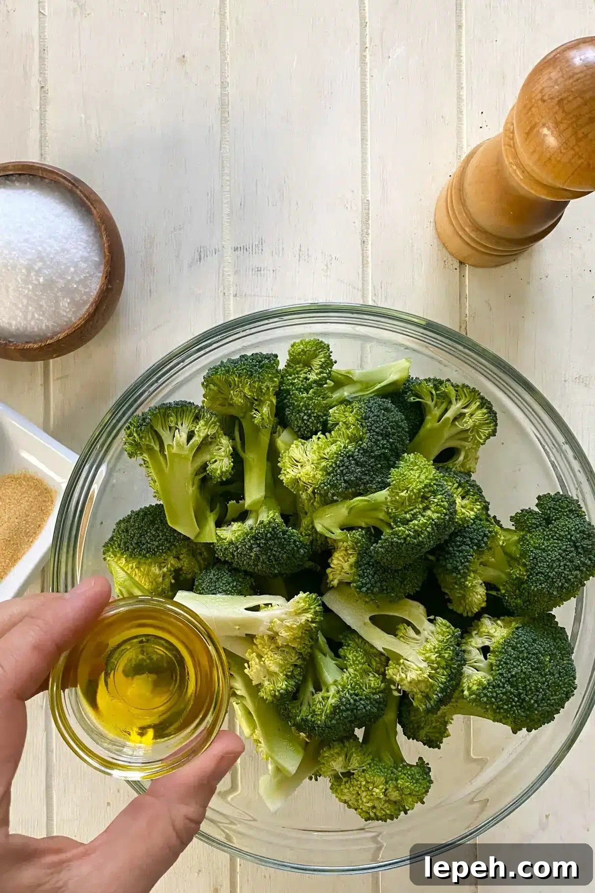 raw broccoli florets in a glass bowl and adding olive oil.