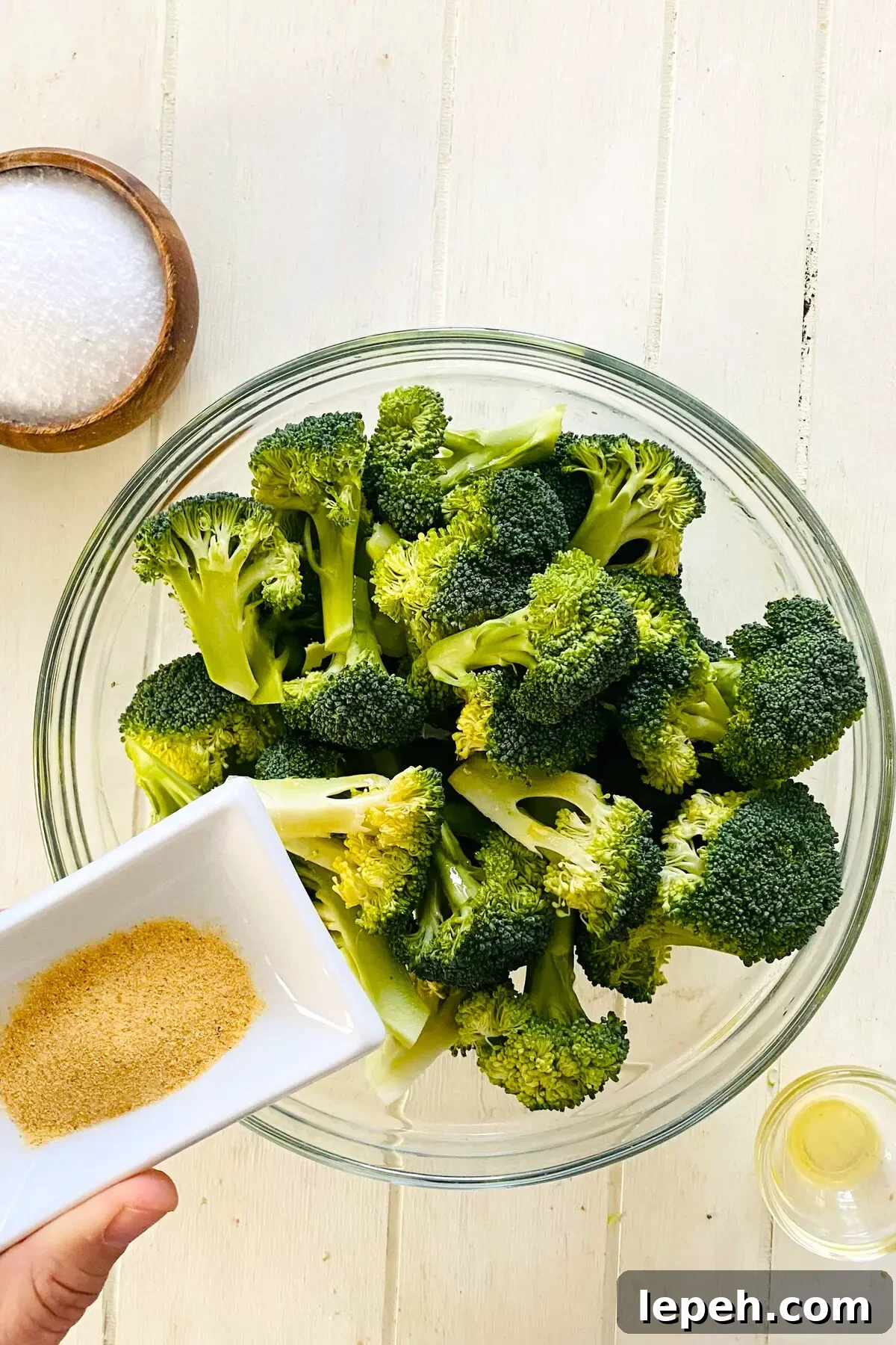 adding garlic powder to raw broccoli.