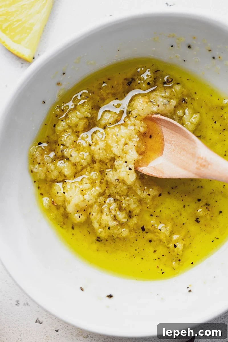 Close up overhead shot of a small bowl with olive oil, grated garlic, garlic powder, salt, and pepper. 