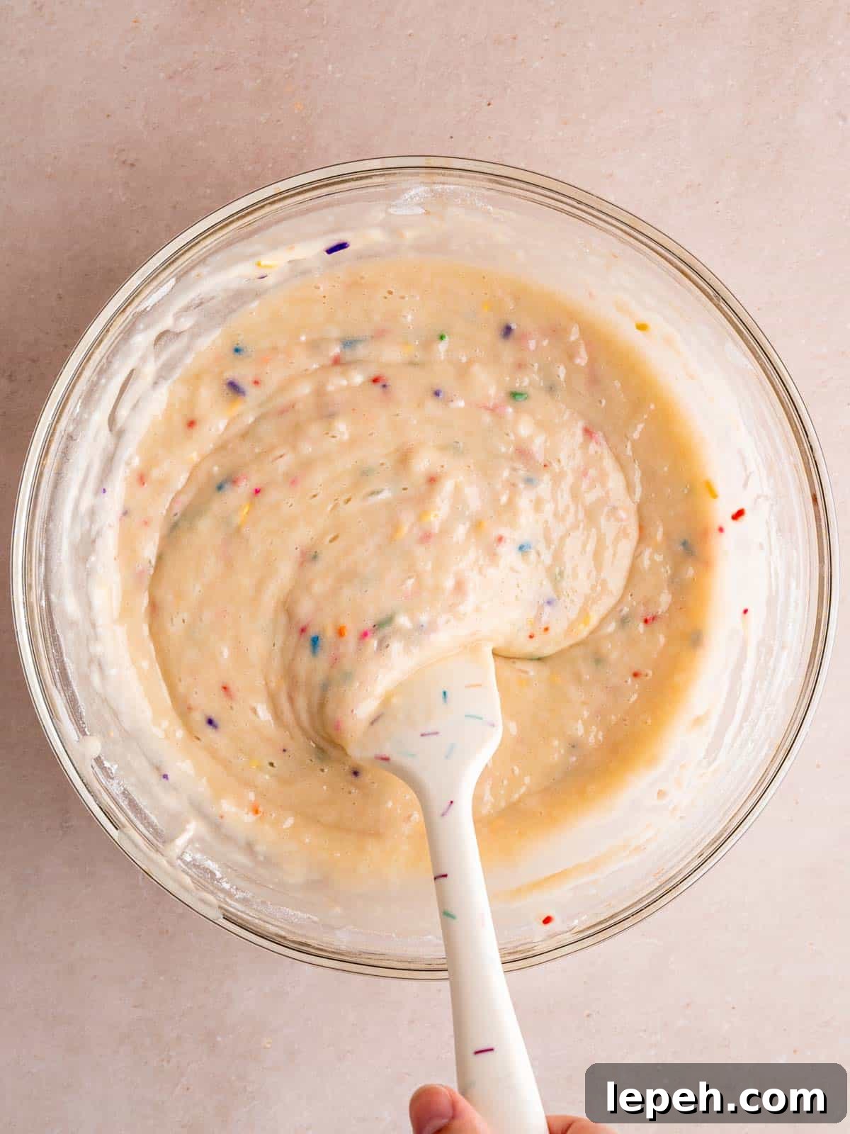 Mixing rainbow sprinkle cake batter in a bowl.