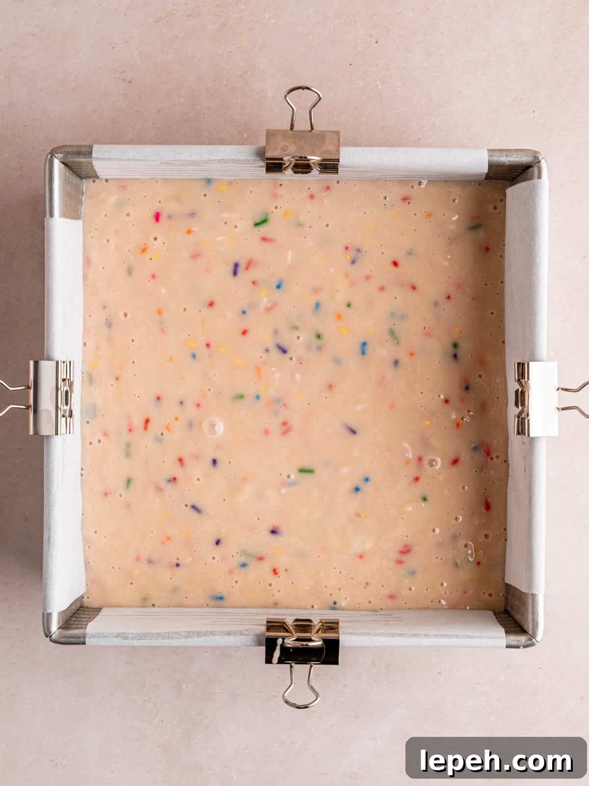 Confetti cake batter in an 8x8 inch pan lined with parchment paper.