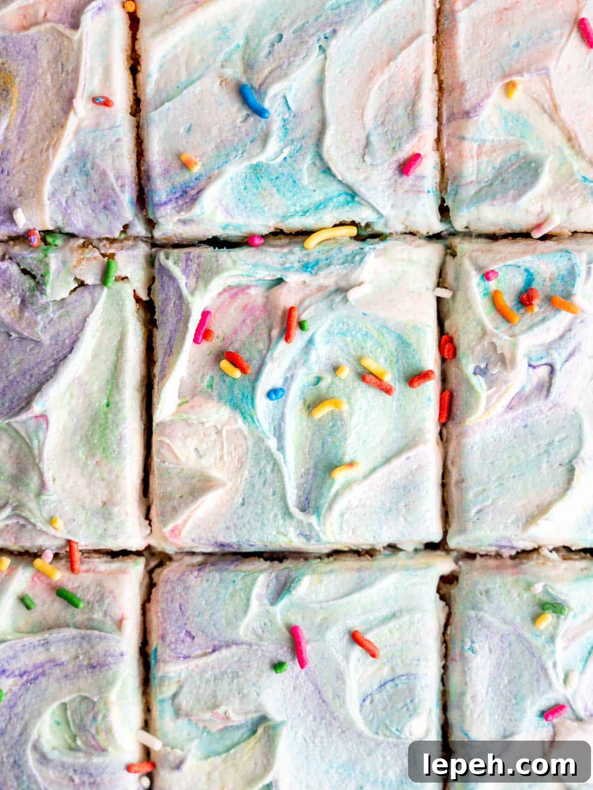 A confetti cake with rainbow tie-dye frosting and sprinkles cut into squares.