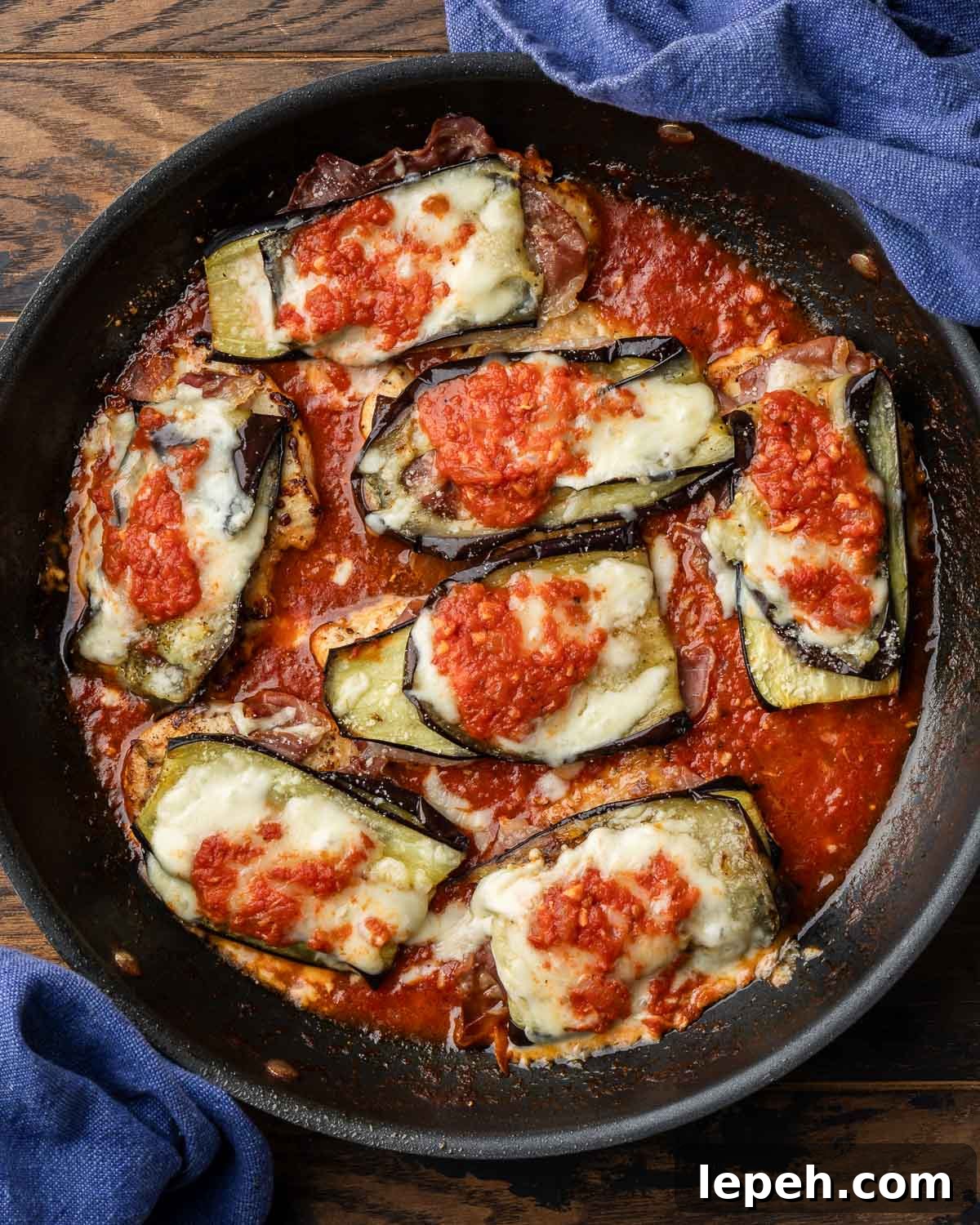 Chicken sorrentino in black pan on wood table.