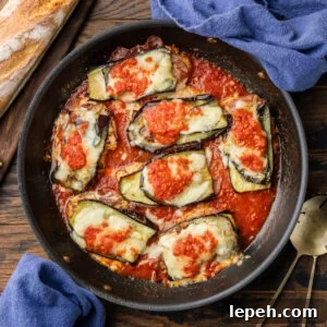 Chicken sorrentino in black pan with blue napkins and loaf of bread.