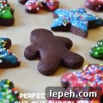 an unfrosted chocolate sugar cookie among frosted chocolate sugar cookies on brown parchment