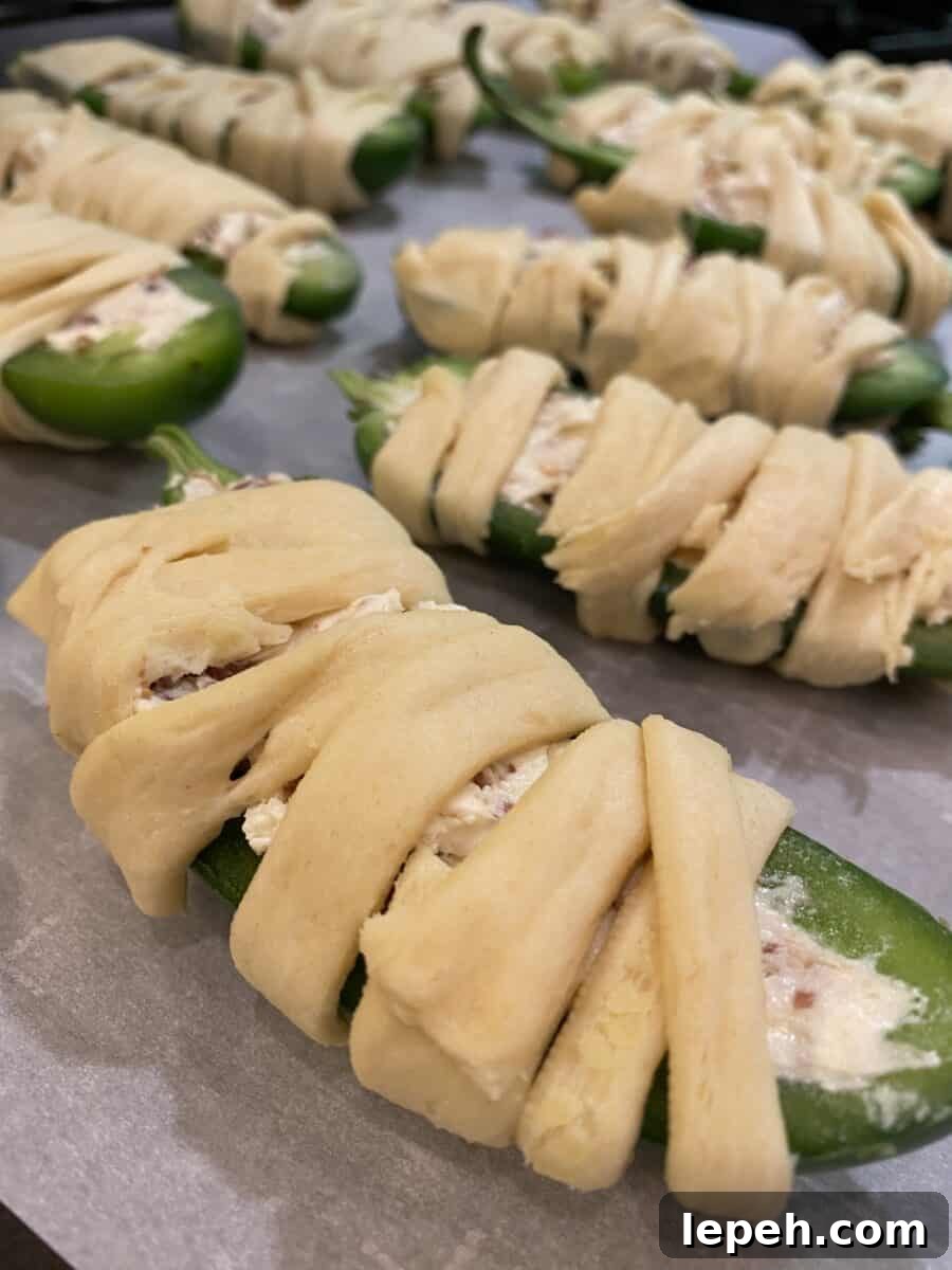 Unbaked jalapeño halves wrapped in crescent dough on a baking sheet.