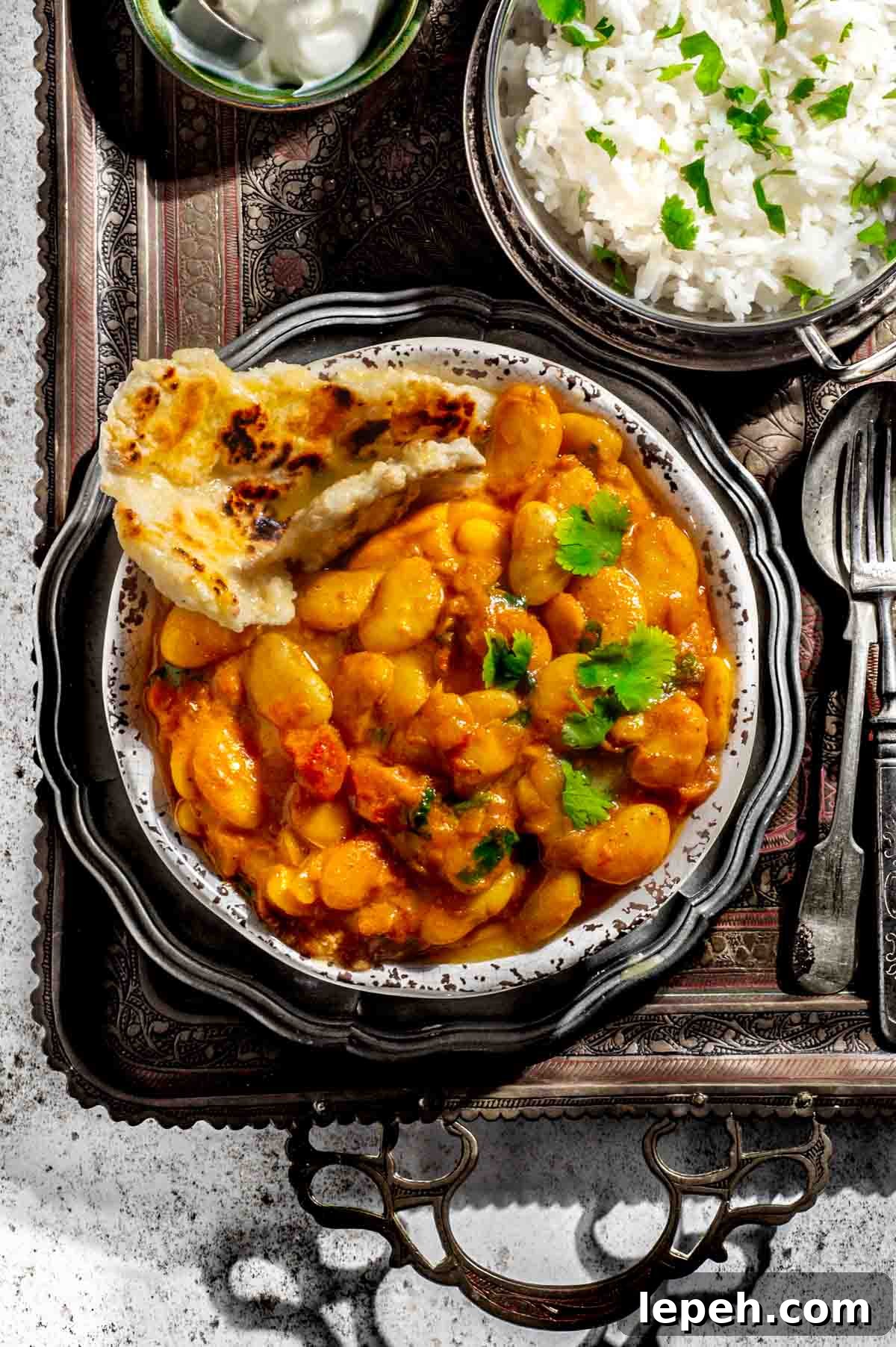 Butter bean curry in a bowl alongside a bowl of rice and a bowl of yoghurt.