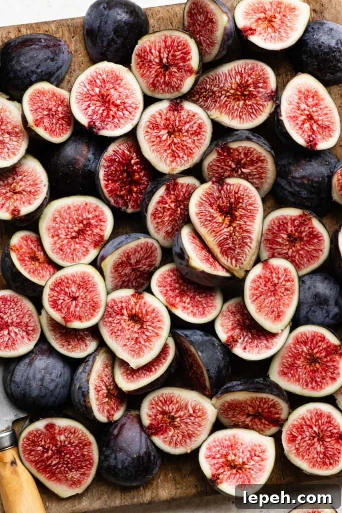 Sliced purple figs with bright pink centers layered on top of each other to cover a cuttingboard.