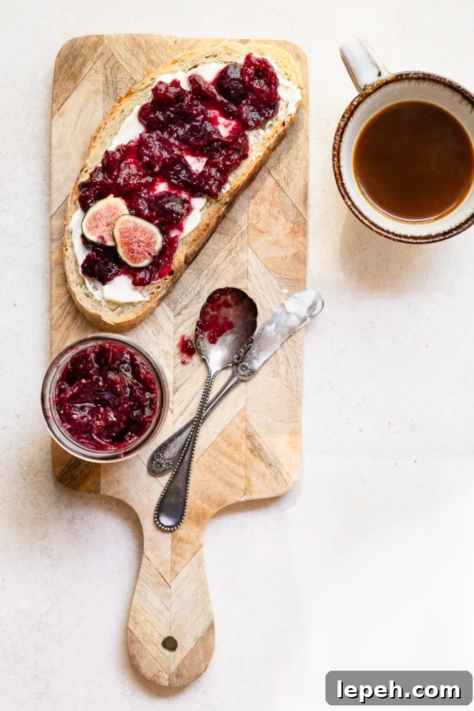 Slice of bread covered in fig jam on a cutting board next to a jar of fig jam and a cup of coffee.