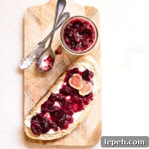 Slice of bread topped with fig jam next to a jar of fig jam on a cutting board.