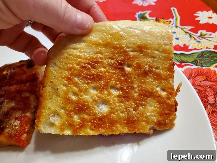 Underside of a slice of grandma pizza showing the burnished golden brown fried bottom crust.