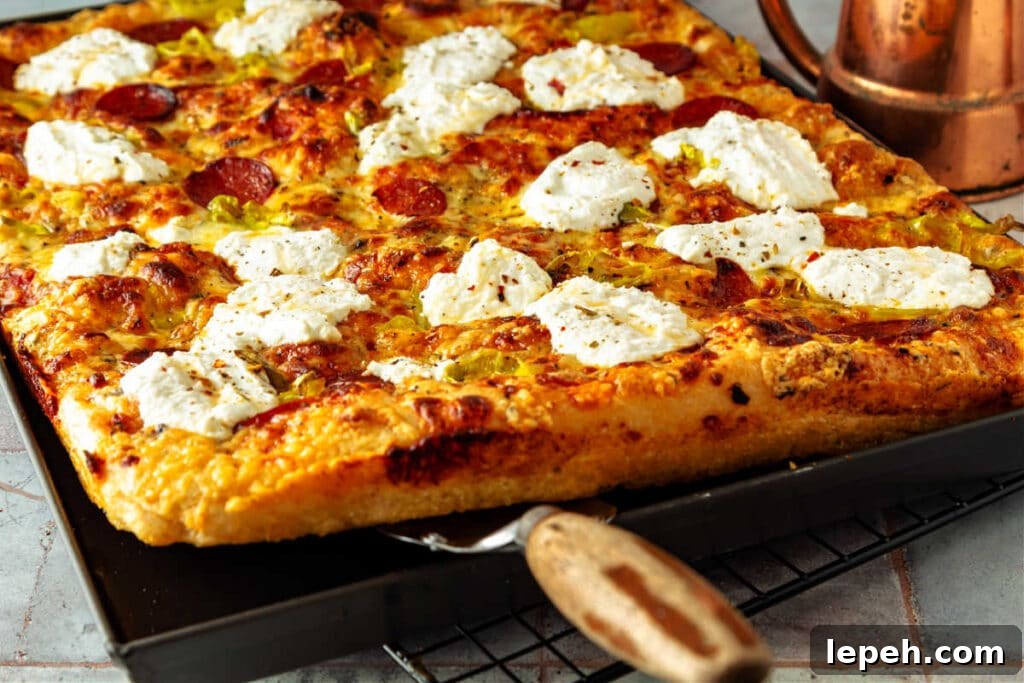 A grandma pizza partly lifted out of its dark gray pan by a spatula.