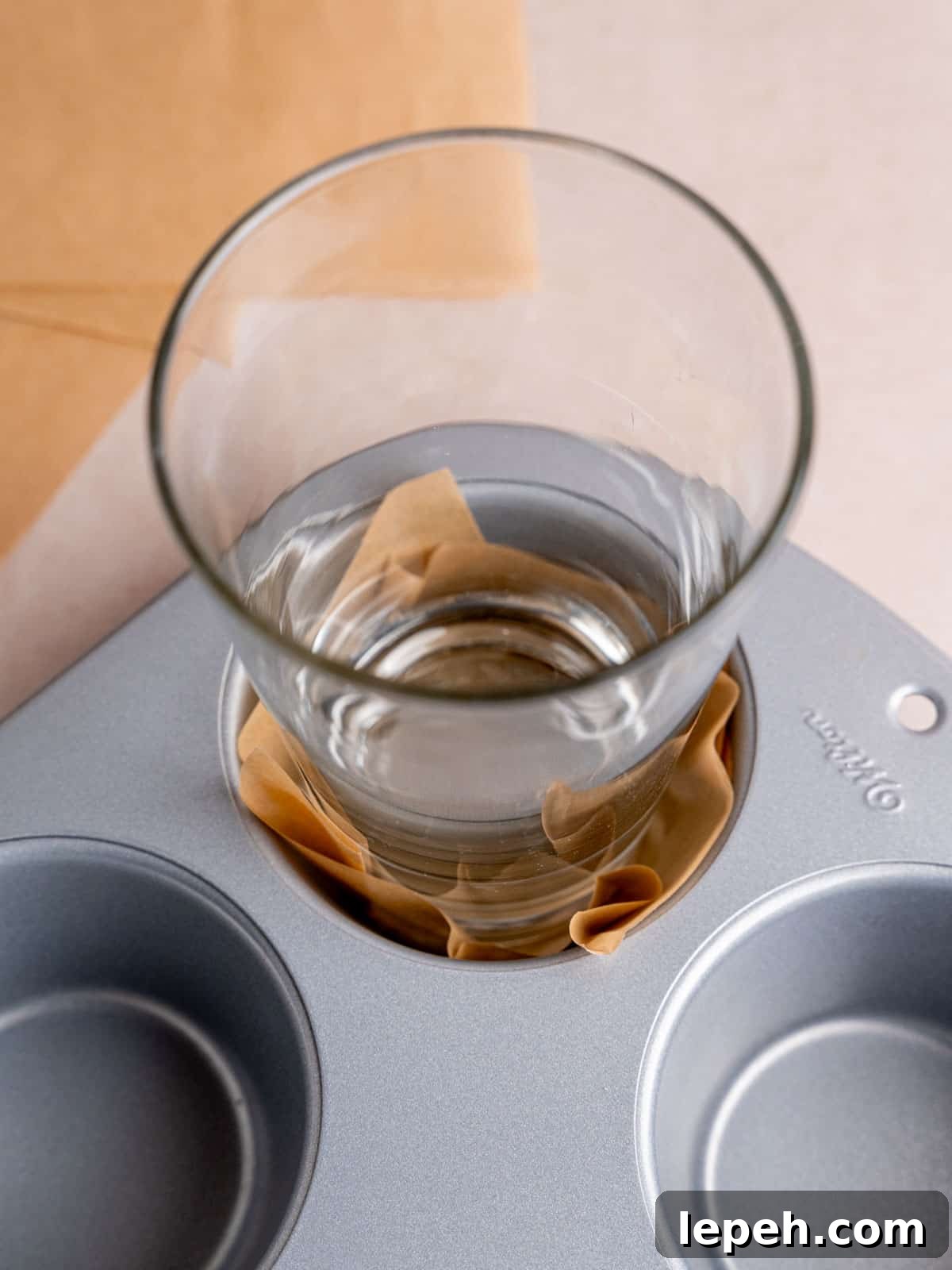 A homemade muffin liner pressed into a pan with a glass.