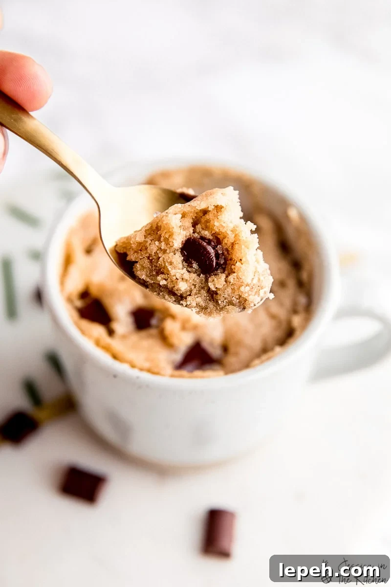 Close up of a spoonful of tahini chocolate chip mug cake with a mug in the background.