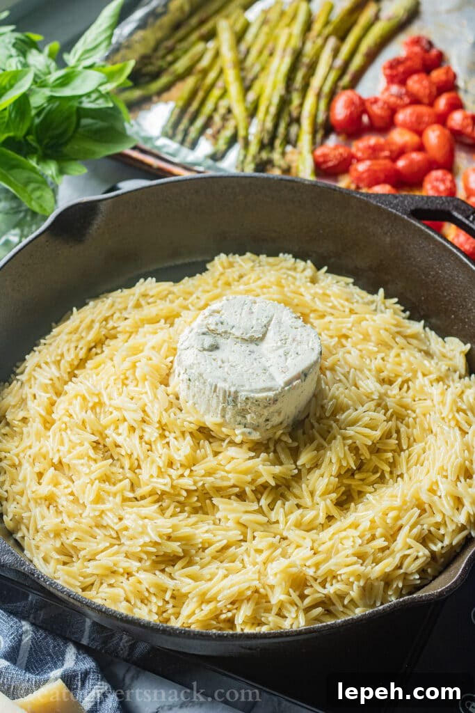 Cooked orzo in a pan with boursin cheese on top.