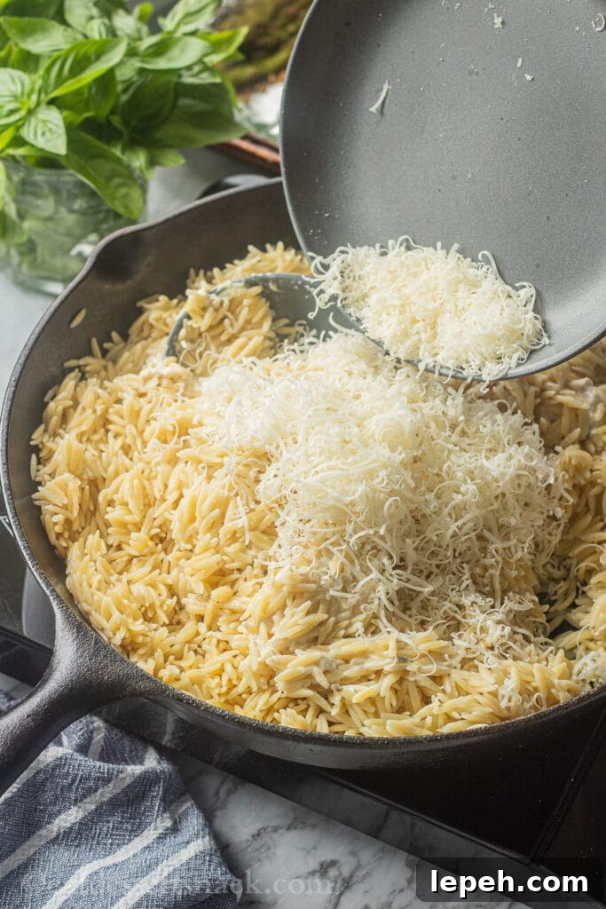Pouring grated parmesan cheese onto cooked orzo.