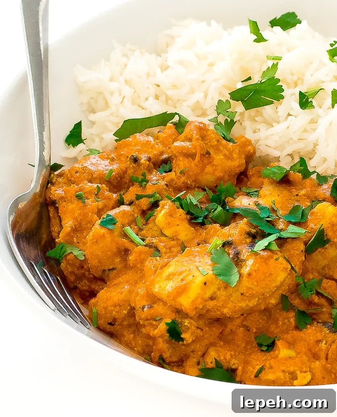 Chicken Tikka Masala in a white bowl with white rice and a fork.