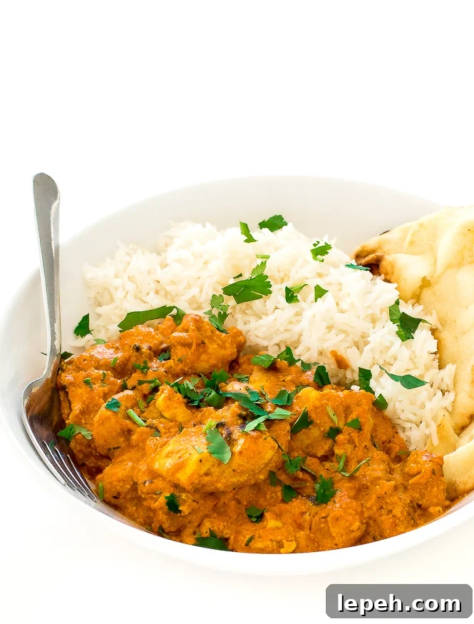Chicken Tikka Masala in a white bowl with white rice, naan, and a fork.